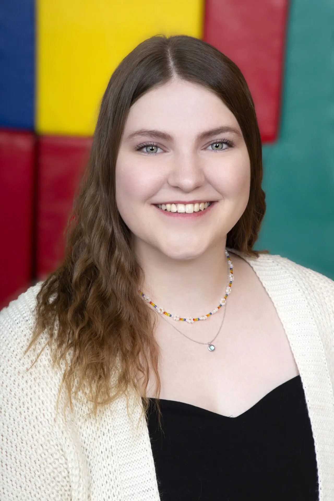 Josephine Schulze-Bisping mit lächelndem Gesicht, trägt eine schwarze Bluse und eine helle Strickjacke, vor buntem Hintergrund.